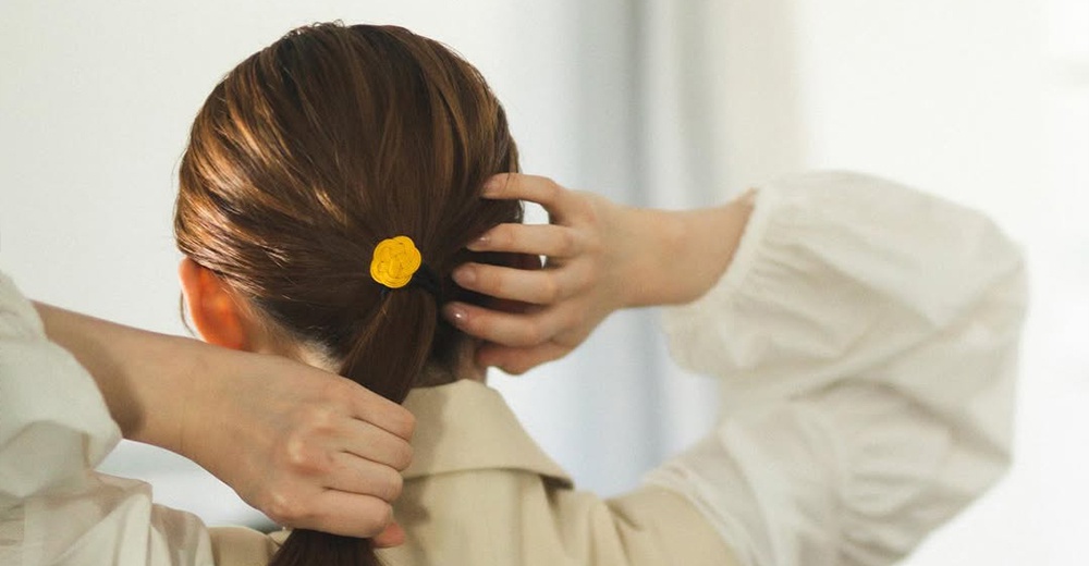 黃色水引花結髮圈，以手工編織而成，固定於棕色頭髮紮成的馬尾上。