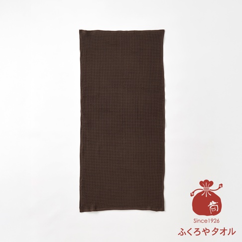 深棕色格紋毛巾，右下角有紅色吉祥物圖案與日文標誌