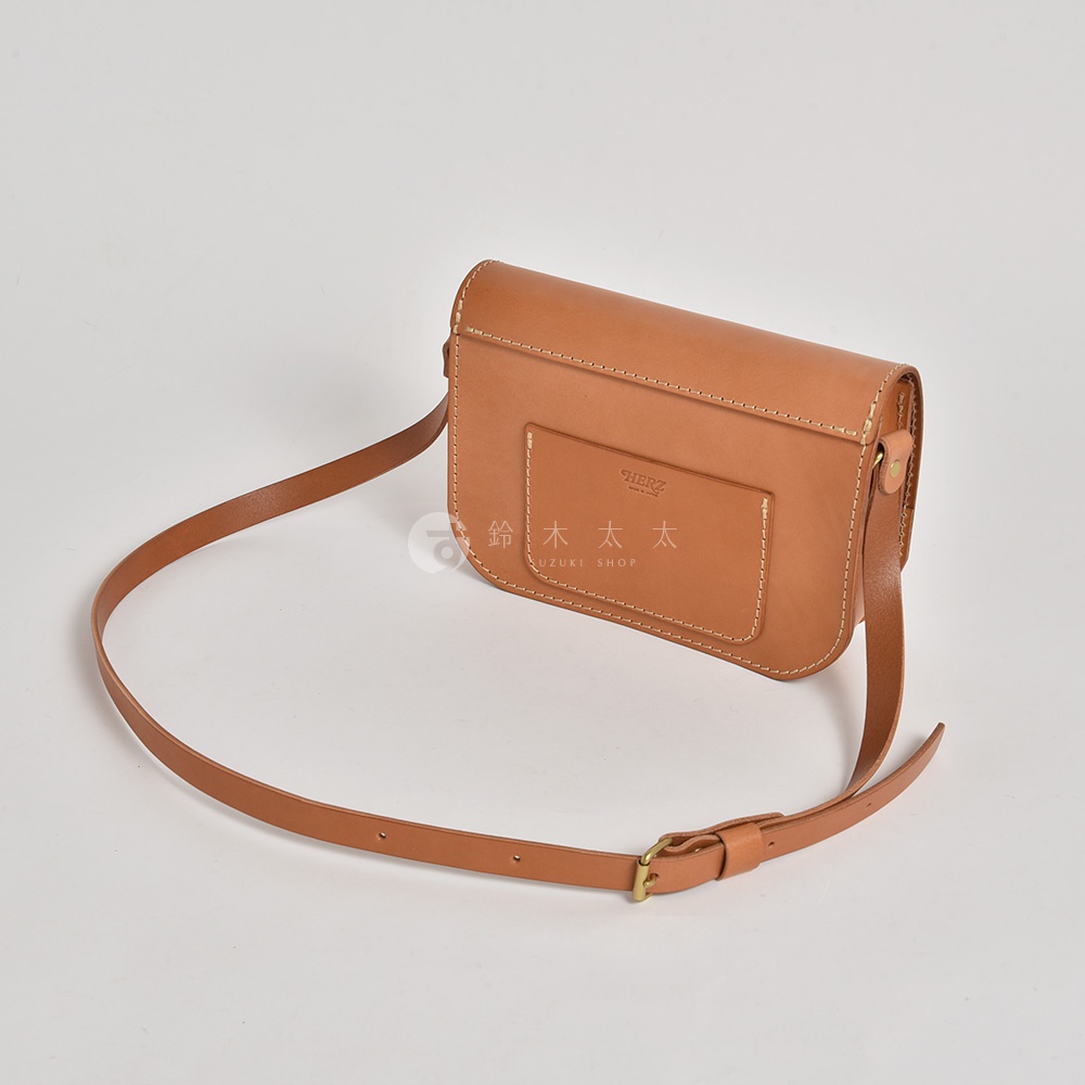 職人手作皮革翻蓋橫式單肩包，採用淺棕色皮革製成，包款帶有品牌標誌的方型前袋，並配有可調節長度的細肩帶。
