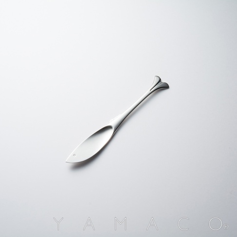 一個銀色不鏽鋼奶油抹刀，造型如魚，握柄末端有兩片葉狀設計，置於純白背景上。