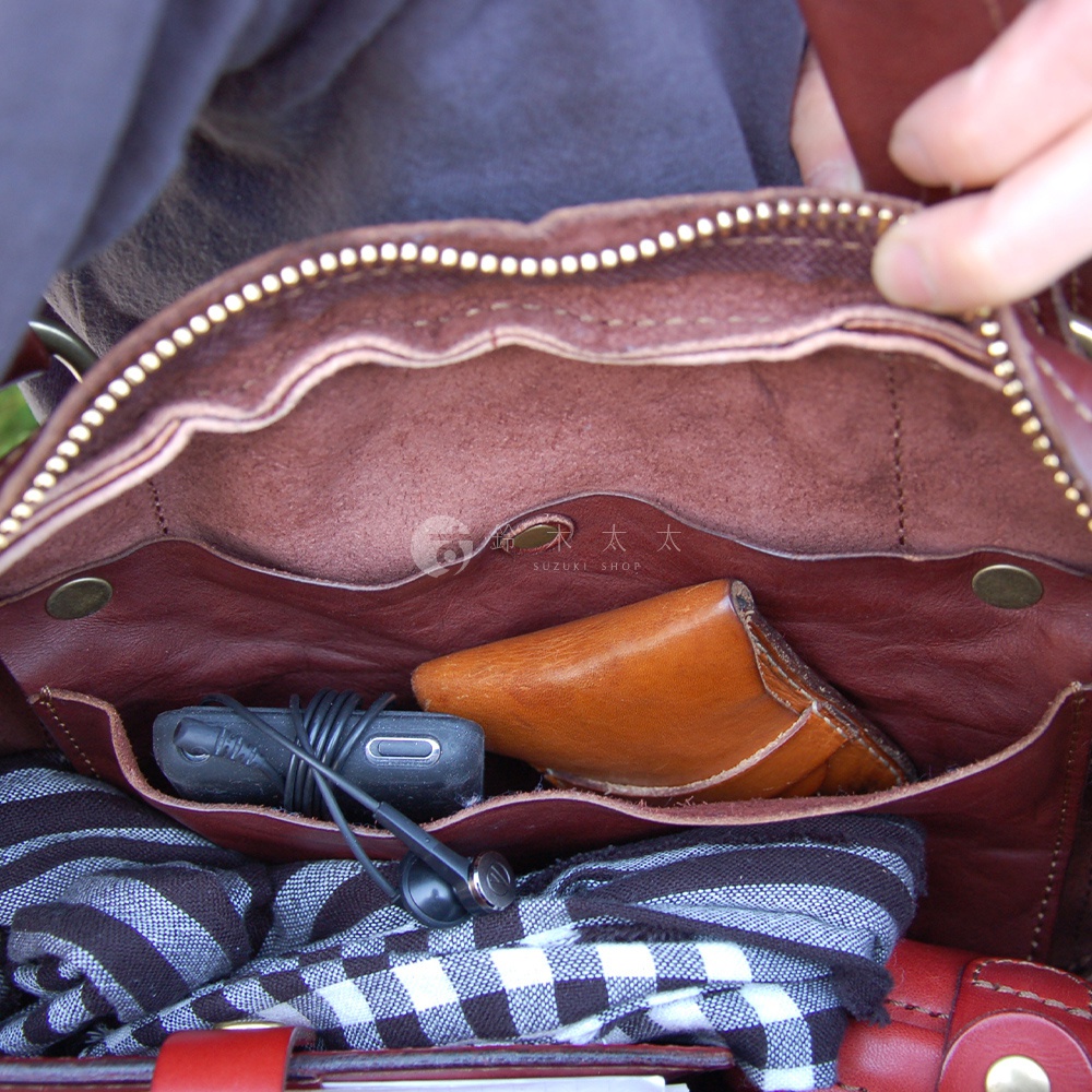 職人手作皮革水洗加工迷你波士頓包內部，露出棕色皮革內襯、拉鍊、手機、耳機及格紋布料。