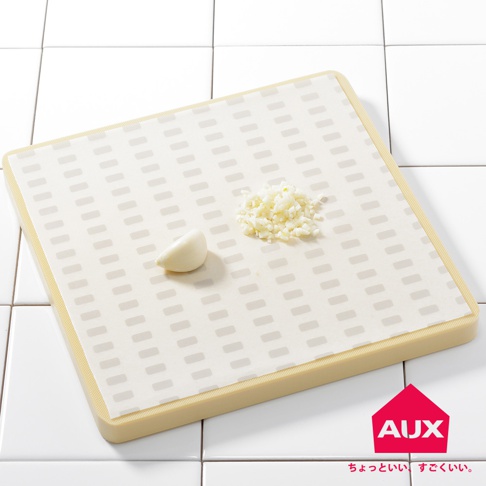 米白色紋路砧板防汙紙，上面放著一瓣大蒜和一小撮切碎的蒜末，砧板邊緣為淡黃色。