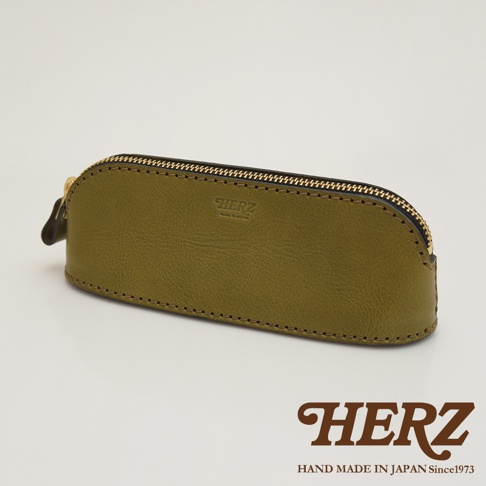 橄欖綠皮革製的職人手作三角弧形收納筆袋，配有金色拉鍊和黑色滾邊，表面壓印有「HERZ」品牌標誌。