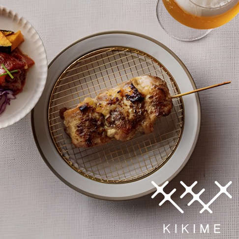 美濃燒瀝油餐盤，盤面為淺灰色，盤緣有白色飾邊，盤中置有金色網架，網架上放著一串烤雞肉串，雞肉呈金黃色，表面有烤過的痕跡。