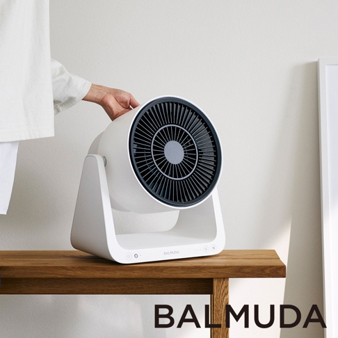 Balmuda GreenFan C2 循環扇，白色機身搭配黑色扇網，圓形扇葉設計，座立於木質桌面上，左側有人手觸碰。