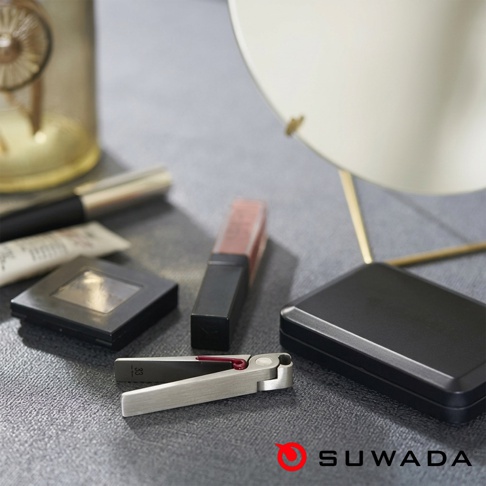 質感細緻的 SUWADA 日本職人 Petite 波堤指甲剪平放於桌面，機身呈現金屬霧面光澤，剪口處飾有紅色細節。周邊圍繞著美妝小物、黑色方形粉盒及鏡子，整體畫面呈現簡約精緻的現代感氛圍。