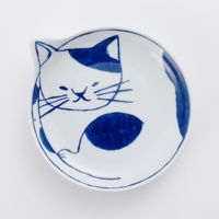 一個白底藍花的陶瓷小碟，繪有簡約的貓咪圖案，貓咪的臉部和身體呈現可愛的蜷縮姿態，藍色筆觸描繪出貓咪的耳朵、眼睛、鬍鬚、斑紋和尾巴，碟子邊緣略微上翹，造型獨特。