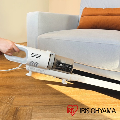 白色輕量有線吸塵器，配有透明集塵筒和灰色手把，正被用於清潔木地板，靠近淺灰色沙發。