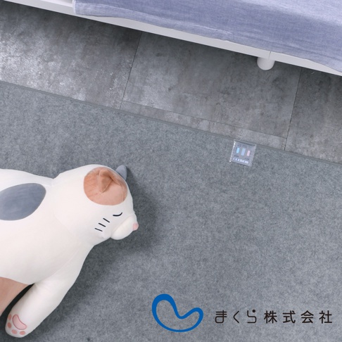 灰色細絨布質地的單人備長炭防潮床墊，上置一個白色、帶有灰色斑紋及粉色腳掌的貓咪造型絨毛玩偶。