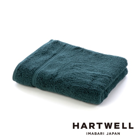 一條摺疊的深藍綠色毛巾，質地蓬鬆柔軟，邊緣有裝飾條紋。