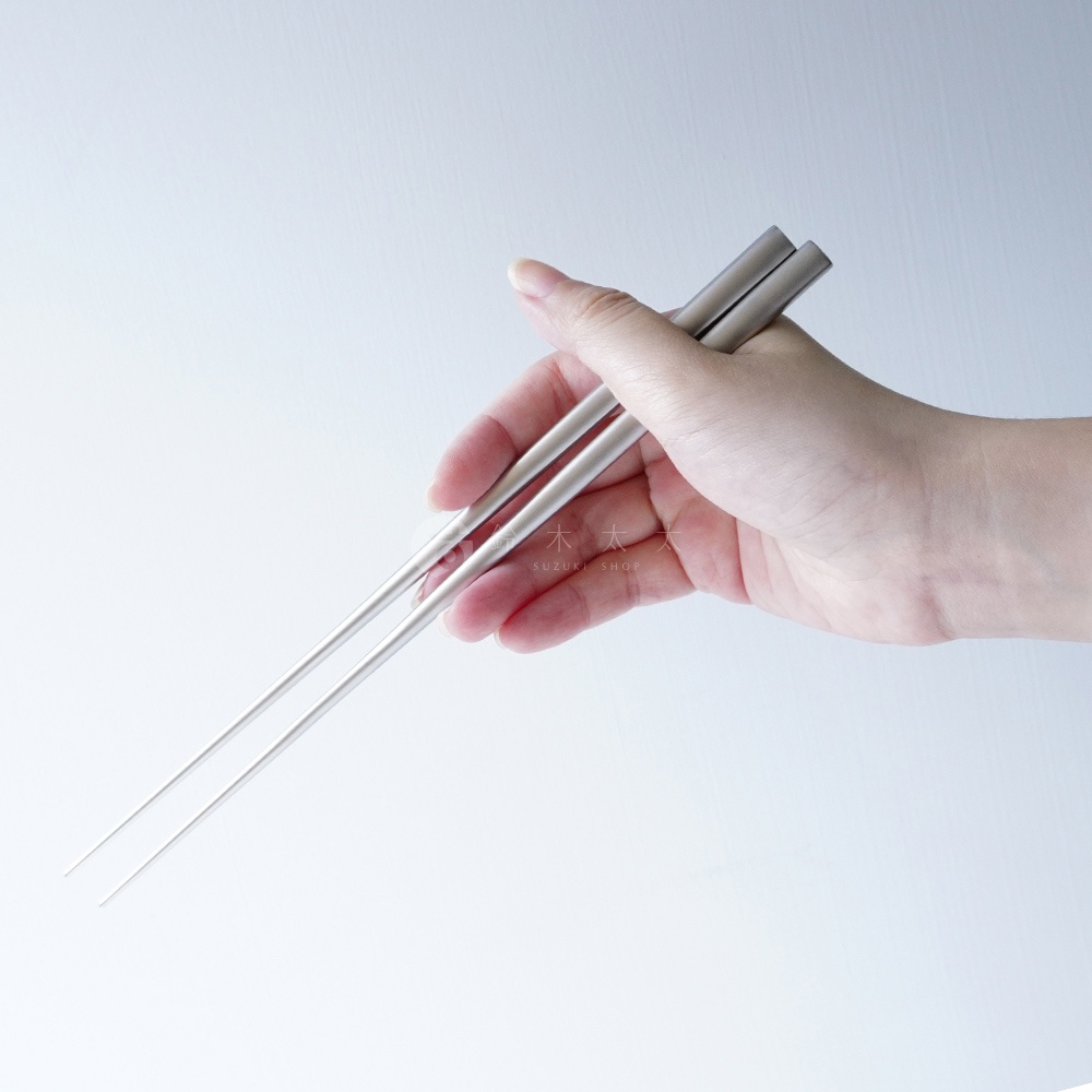 燕三条不鏽鋼筷，一雙為22.3公分長，呈現銀色金屬光澤，筷身筆直，末端尖細，由手持展示。