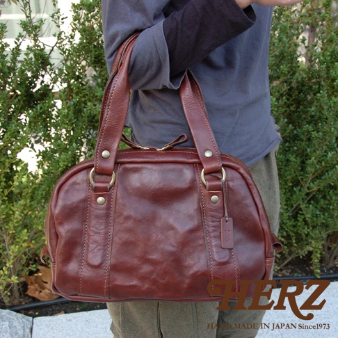 職人手作皮革迷你波士頓包，呈現深棕色，採用水洗加工皮革製成，帶有復古質感，配有雙提把和金色五金配件。