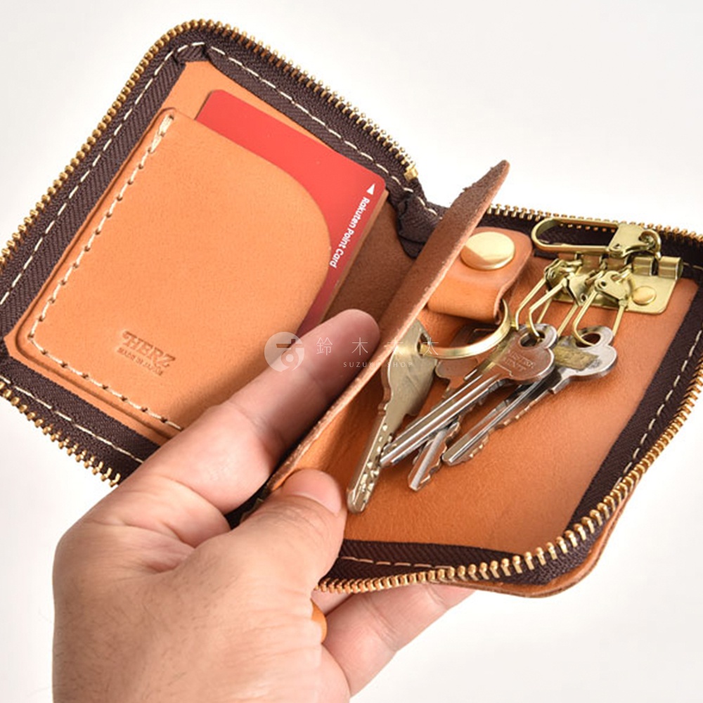 職人手作皮革多用途收納鑰匙包，採用 tan 色皮革，內含多把鑰匙及一張信用卡，並有拉鍊封口及品牌標誌。