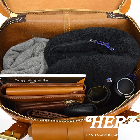 棕色皮革旅行後背包內部，裝有灰色毛衣、黑色刷毛外套、皮夾、筆記本和黑色耳機。