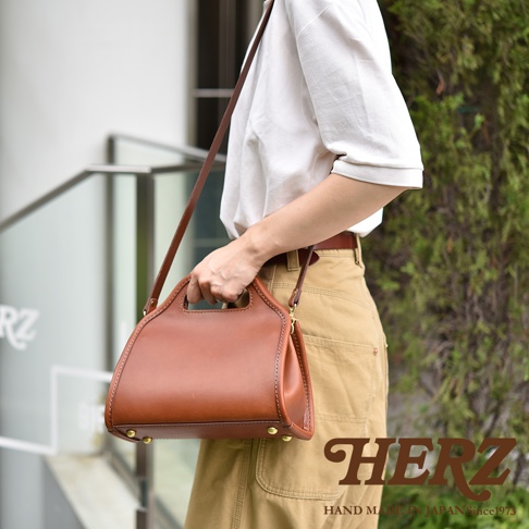 職人手作皮革單肩兩用拱型手袋，採用光滑棕色皮革製成，配有同色系皮革提把和可拆卸肩帶，包身側邊有金屬卯釘裝飾。