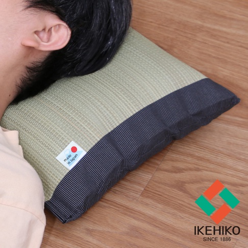 藺草編織的枕頭，表面呈現淺綠色網格紋理，一側邊緣為深藍色條紋布料。枕頭上有「made in Japan」標籤。