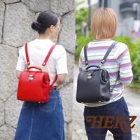 兩位女性各背著一個職人手作皮革迷你後背醫生包，左邊為鮮紅色，右邊為黑色。包款採用皮革材質，設計經典，帶有金屬鎖扣和提把。