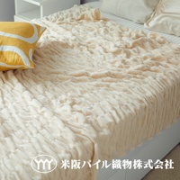 米色絨毛毯，表面有壓紋的蓬鬆織紋，鋪在床上，左側搭配黃色抱枕。