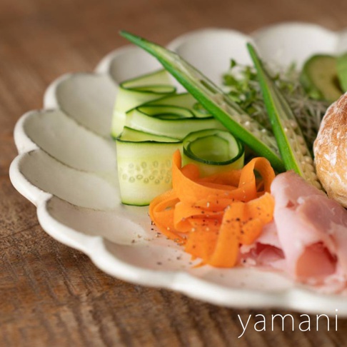 白色陶瓷花型主食盤，盤中擺放著花式切法的黃瓜片、紅蘿蔔絲、秋葵、豆芽菜、火腿和麵包。