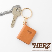 職人手作皮革書本造型鑰匙圈，焦糖色皮革，壓有「HERZ MADE IN JAPAN」字樣，搭配金色鑰匙圈與銀色鑰匙。
