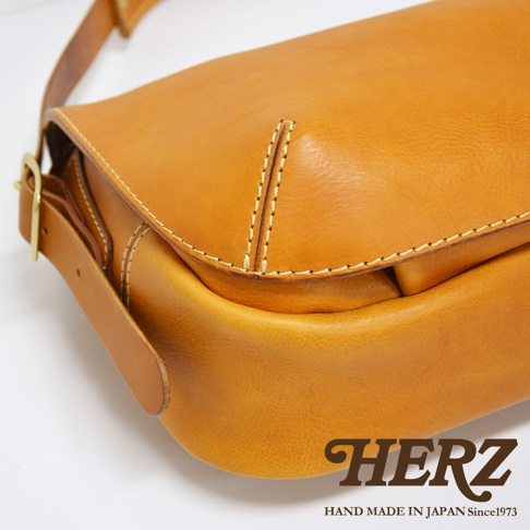 職人手作皮革復古翻蓋郵差包，採用天然皮革材質，呈現溫潤的焦糖棕色。包款設計簡約，細緻的縫線工藝展現職人精神，搭配金屬扣環，風格經典耐看。