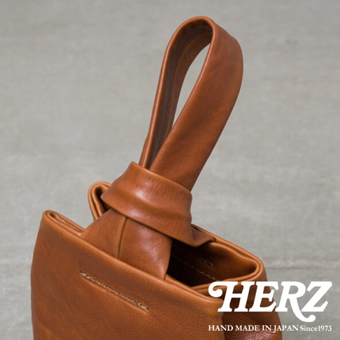 棕色皮革單柄手提包，手柄處有扭結設計，包身皮革紋理清晰，縫線細緻，展現職人手作質感。