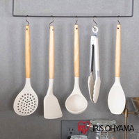 一套白色矽膠廚房用具，包含漏勺、鍋鏟、湯勺、夾子和煎匙，皆配有淺木色手柄，懸掛於黑色掛架上。