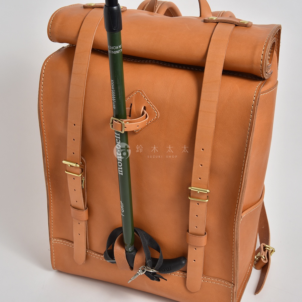 棕色皮革製成的大容量後背包，配有登山杖固定帶和金屬扣環，風格復古，適合戶外活動。