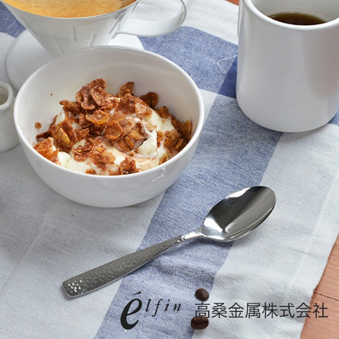 日製錘目紋不鏽鋼水果甜點匙，勺身呈現細緻的錘擊紋理，銀色不鏽鋼光澤，置於白色碗盤與藍白格紋桌布上，旁有咖啡杯與冰淇淋玉米片。