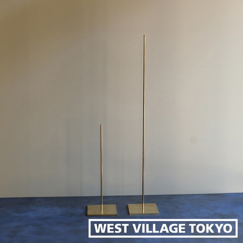兩個黃銅一輪花器/燈具展示架，一個較高，一個較矮，均有方形底座，立於深藍色地面上，背景為淺色牆面。