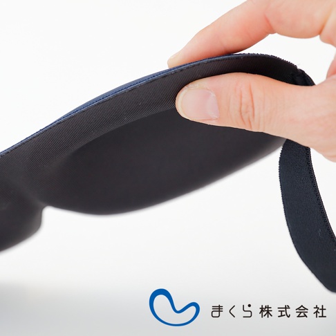 手指輕壓深藍色舒眠眼罩，展現其柔軟的內部填充材質，邊緣有彈性綁帶。