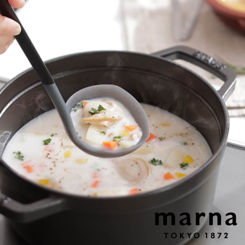 marna TOKYO 1872，手持灰色矽膠湯杓舀起一鍋濃稠的白色奶油海鮮燉湯，湯杓中盛滿湯料，有魚肉、馬鈴薯塊、紅蘿蔔丁和香芹碎，鍋內也同樣有豐富的食材，熱氣蒸騰，一派溫馨的烹飪場景。