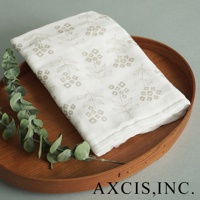 白色純棉花草紗布大拭巾，印有米色花草圖案，平鋪在木質托盤上，旁襯綠色尤加利葉。