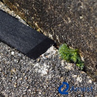 黑色零死角清潔刮刀，長方形，邊緣有細微磨損。刮刀置於粗糙的灰色石質表面，旁邊有一小叢綠色苔蘚。