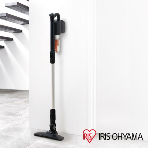 黑色和銀色的輕量無線手持吸塵器，配有透明集塵筒，正掛在白色牆壁上的充電座。吸塵器底部有黑色吸頭，直立於灰色磁磚地板上。