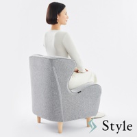 灰色布藝美姿調整座椅，椅背有條紋裝飾，搭配木質椅腳，一位身穿白色上衣和米白色褲子的女性側坐其中。