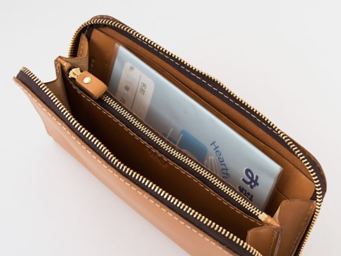 職人手作皮革長夾，淺棕色牛皮材質，設有多個隔層，拉鍊開合，內有藍色小冊子。