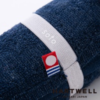 深藍色毛巾捲起，上面繫著白色鬆緊帶，鬆緊帶上有soto字樣，旁邊有一個紅色小標籤，標籤上有圓圈和藍白條紋。