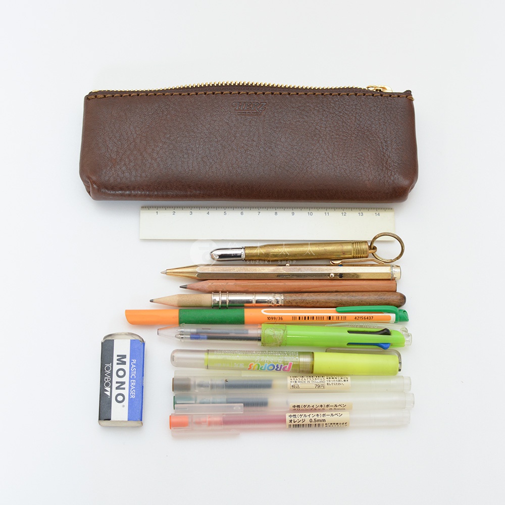 深棕色皮革筆袋，配有金色拉鍊，旁邊擺放著一支金色筆、一支鉛筆、兩支鋼筆、一支螢光筆、一支筆和兩支透明筆，以及一個藍色橡皮擦。