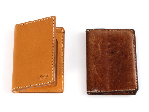 左側是全新淺棕色皮革雙折票券收納夾，右側是使用過的深棕色皮革票券夾，兩者皆以白色縫線裝飾。