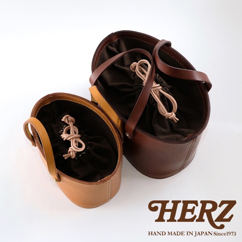 兩款皮革束口手提包，左邊為淺棕色，右邊為深棕色，均為職人手作，內襯為深色布料，束口處有淺色繩結。