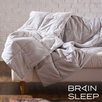 一張淺灰色雙人調溫被，表面有菱形格紋縫製，被子鋪蓋在米白色沙發上，背景為白色磚牆。