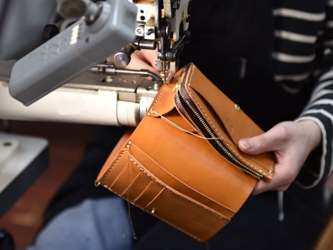 職人手作皮革中型雙折短夾，展現其經典棕色皮革質感，縫線精緻，並配有黃銅色拉鍊與按扣，展現製作過程的細膩。