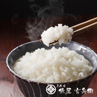 一碗熱騰騰的北海道夢美人米，米粒飽滿潔白，散發著誘人蒸汽。筷子夾起一撮米飯，展示其顆粒分明的質地，碗身為深灰色帶有條紋設計。