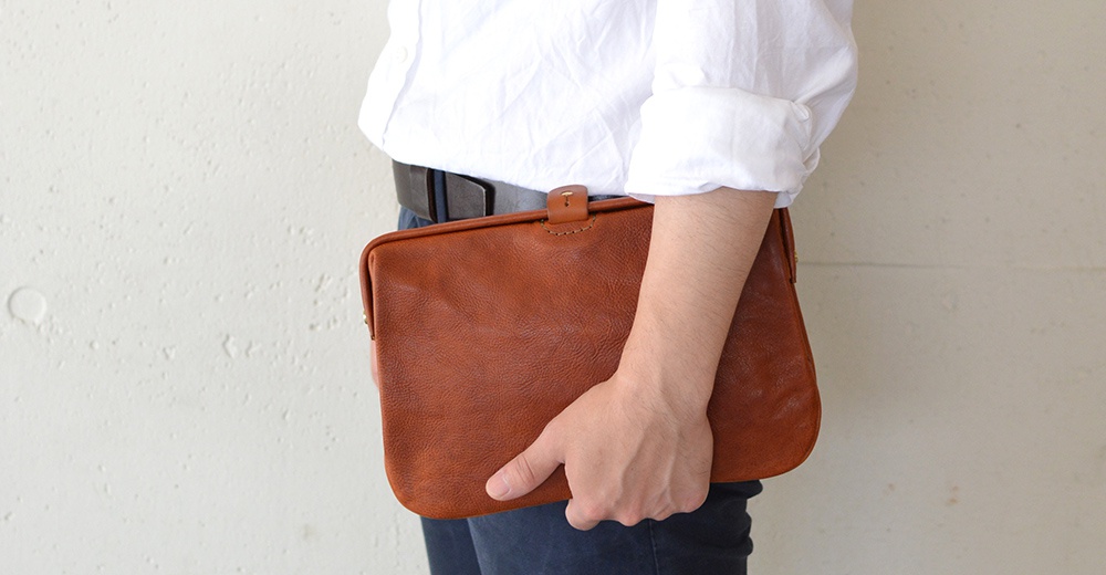 棕色皮革手拿包，帶有皮革按扣閉合，由手持。