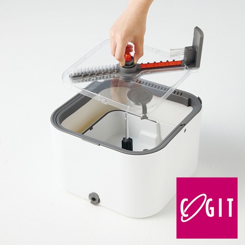 一隻手正將透明蓋子安裝在方形白色水桶上方，蓋子中央帶有旋轉軸心與刷毛結構，水桶內部設有分隔槽與中心轉桿，右下角印有桃紅色背景的COGIT品牌標誌，整體呈現簡約的清潔用品結構。