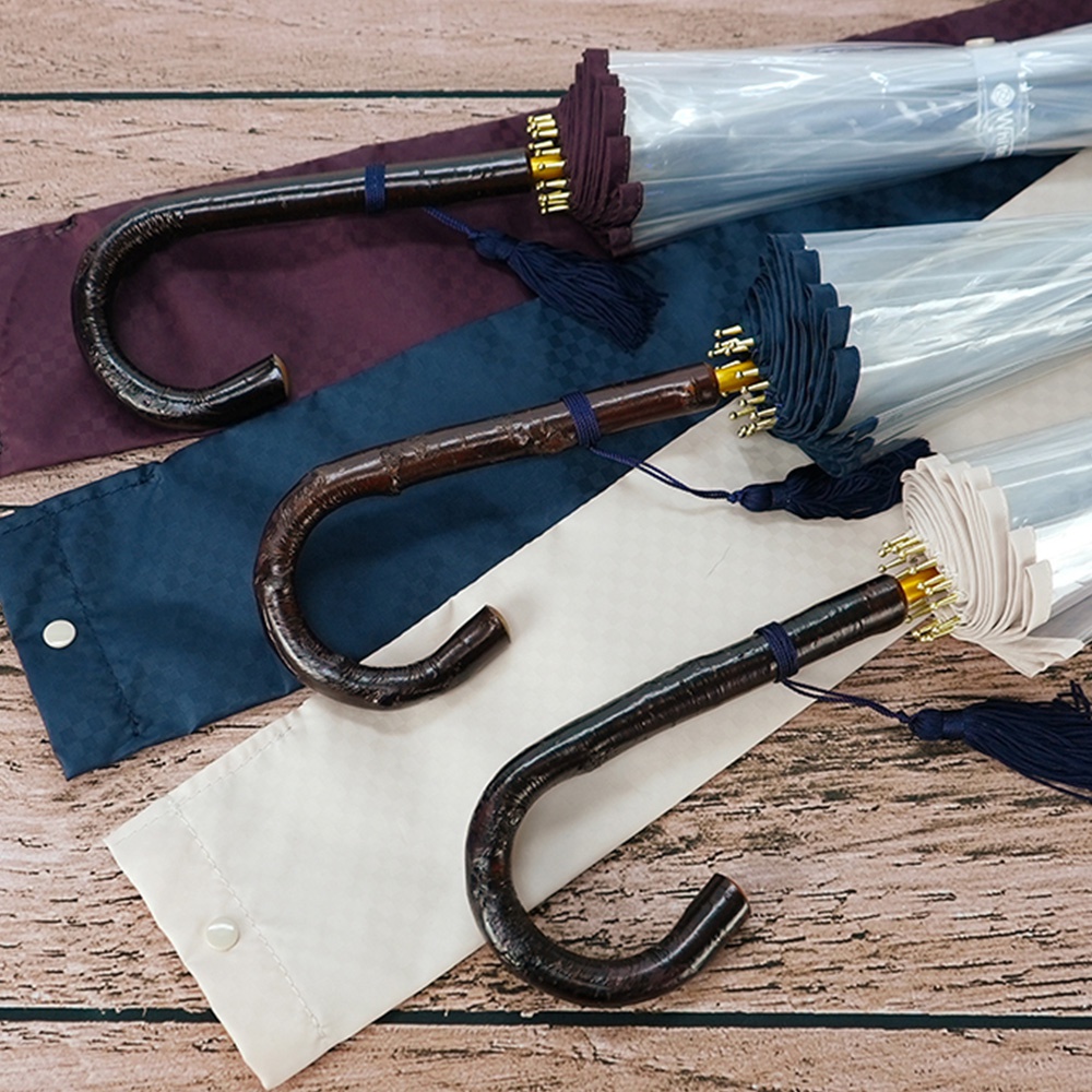 三把職人高級樺木透明傘，傘柄為深棕色彎曲木質，傘下有深藍色流蘇及同色系傘套，傘布為透明材質，傘骨和傘頂為金色。