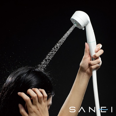 白色兩段式水流蓮蓬頭，由女性手持，水柱從蓮蓬頭噴灑而出，落在黑色頭髮上。