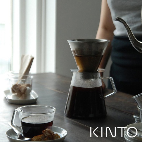 玻璃咖啡壺組，含透明玻璃壺身、帶有銀色金屬濾網的濾杯，以及一個裝有咖啡的玻璃杯，旁邊有方糖和餅乾。