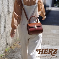 職人手作皮革復古杜勒斯手提包，採用棕色皮革製成，設有金屬鎖扣及可調節肩帶，包身圓潤，側邊飾有金屬铆釘。